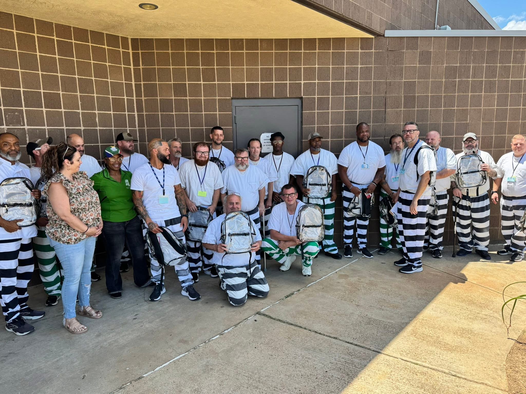 Large group outdoors holding clear backpacks distributed to education program participants at CMCF