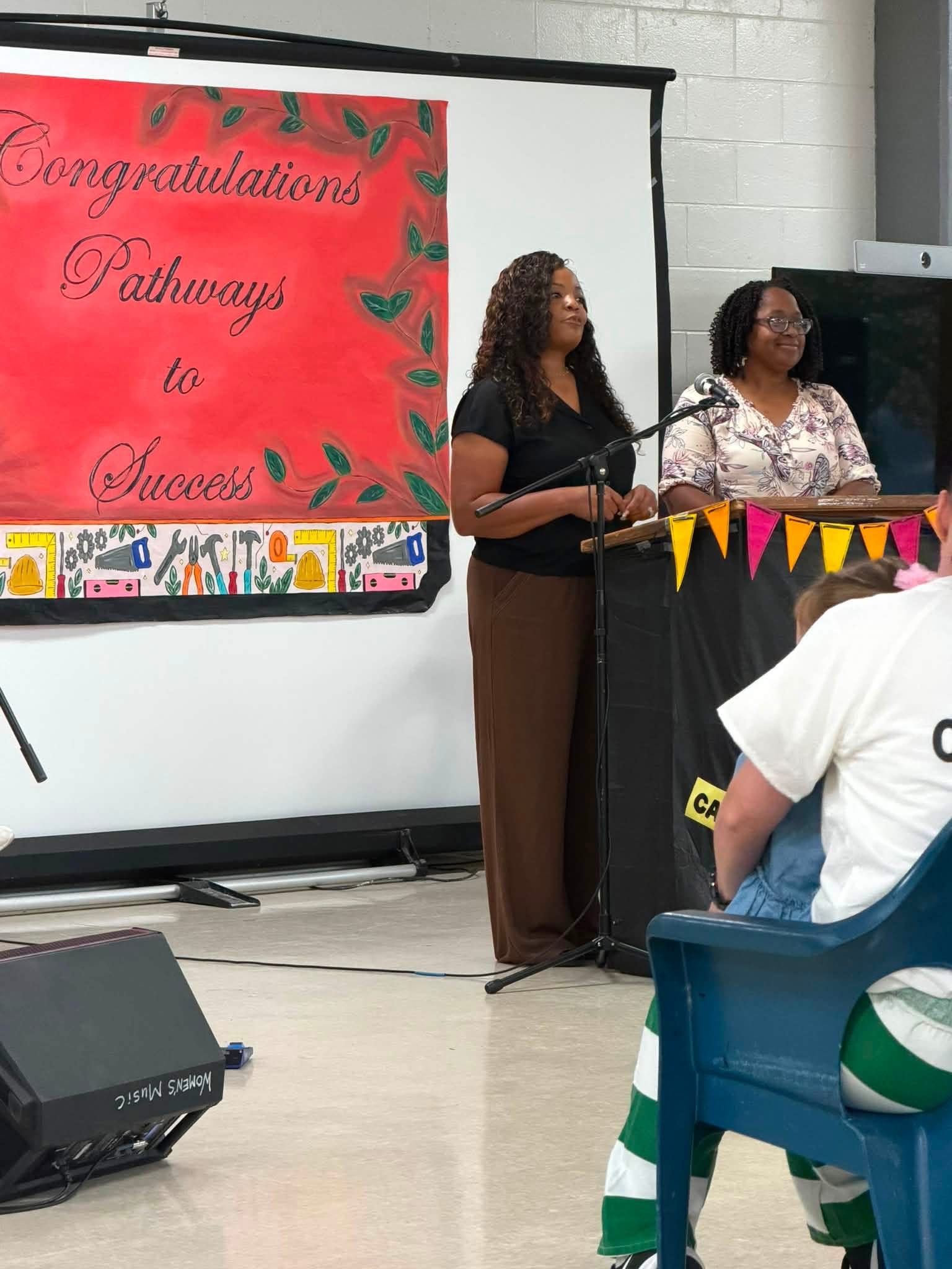 Two speakers at the podium beside the red Congratulations Pathways to Success banner at CMCF